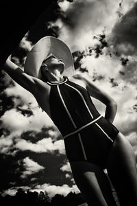 A portrait of a woman in a swimsuit, hat and sunglasses in summer on the riverbank against the sky