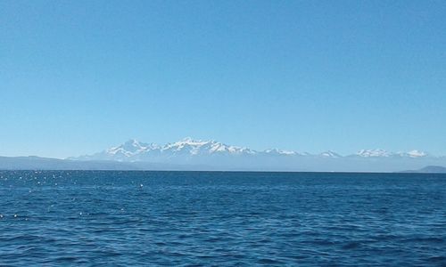 Scenic view of sea and mountains against clear blue sky