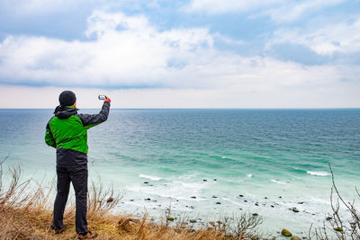 Traveler man with phone camera takes photo of windy sea on coast.