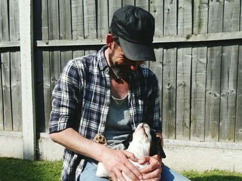 Man holding dog against fence