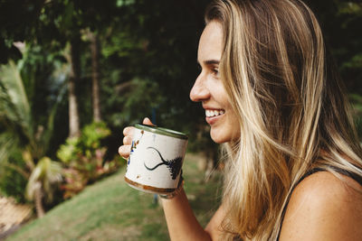 Side view of smiling woman having drink in yard