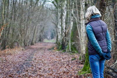 Rear view of woman standing by leaves covered road