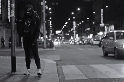 Full length of woman standing on sidewalk by pole in illuminated city