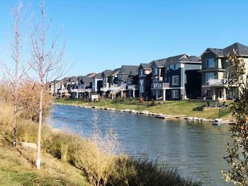 Buildings by river against clear blue sky