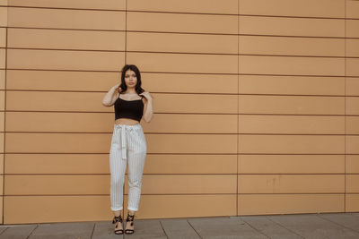 Full length of fashionable young woman standing against wall