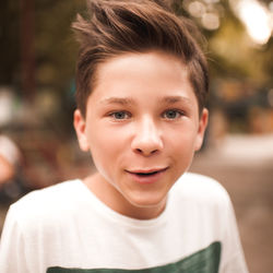 Handsome blonde funny teen boy 14-16 year old with stylish hairstyle posing outdoors close up.