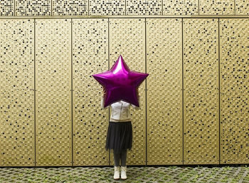 Woman holding pink star shape while standing against wall