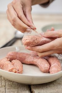 Cropped image of hand holding peeling sausage in bowl