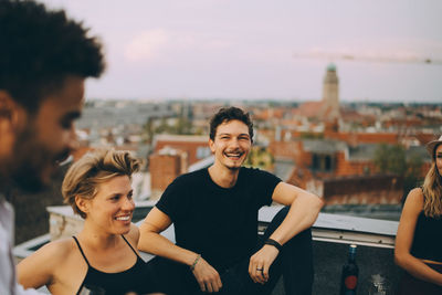 Happy friends enjoying at rooftop party against cityscape