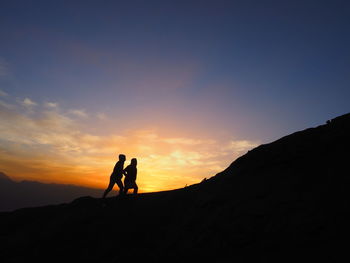 Silhouette men standing on mountain against sky during sunrise