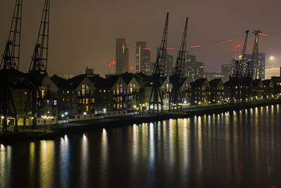 Illuminated buildings by river against sky at night