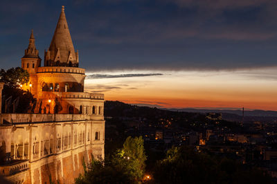 Illuminated buildings in city against sky during sunset