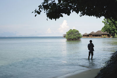 Rear view of man standing in sea against sky