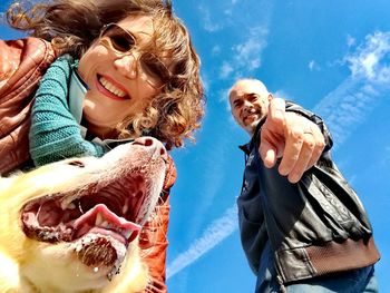 Low angle portrait of man and woman with dog against sky