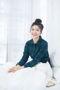 Portrait of smiling young woman sitting on bed at home