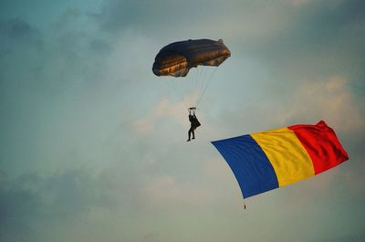 Low angle view of man paragliding with romanian flag against sky