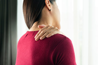 Rear view of woman touching shoulder at home