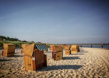 Hooded beach chairs on sand against sky