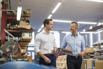 Two businessmen walking and talking in factory storeroom