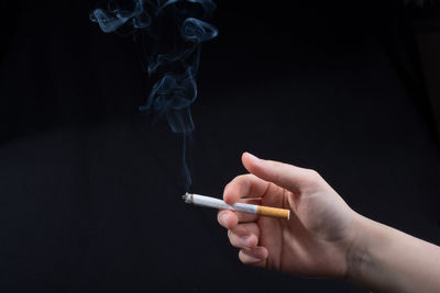 Cropped image of hand holding cigarette against black background