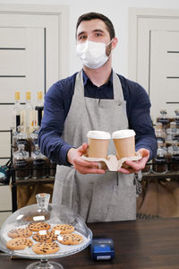 Barista serving coffee in takeaway cups in coffee shop in protective mask. coffee to go during