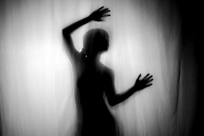 Silhouette woman with arm raised seen through curtain at home