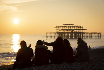 Friends sitting at beach against sky during sunset