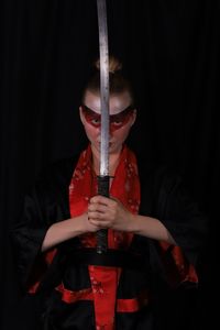 Portrait of man in traditional clothes holding sword over black background