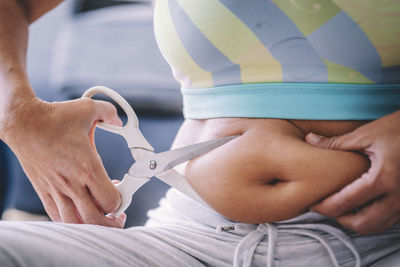 Midsection of woman cutting belly fat with scissors