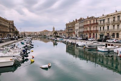 Sailboats moored on canal amidst buildings in city against sky