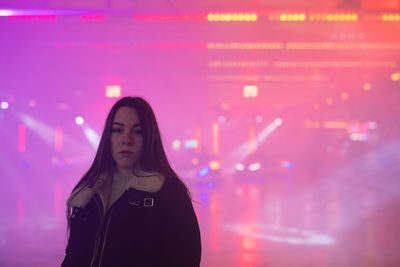 Portrait of young woman standing against illuminated light at night