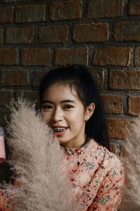 Portrait of smiling young woman with feathers against brick wall