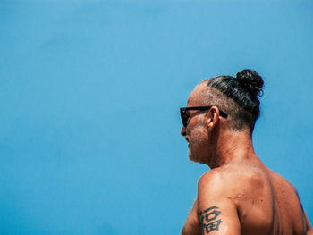 Portrait of shirtless man looking away against blue sky