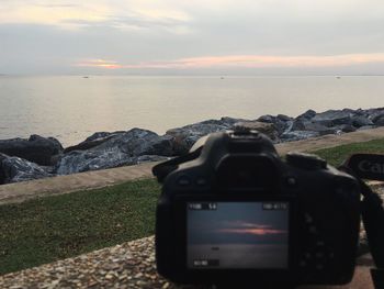 Camera on rock by sea against sky during sunset