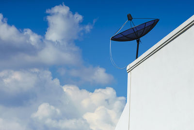 Low angle view of satellite dish on retaining wall against cloudy sky