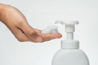 Close-up of hand holding bottle against white background