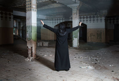Rear view of woman with arms outstretched standing in abandoned building