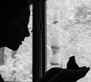 Portrait of silhouette woman looking through window at home