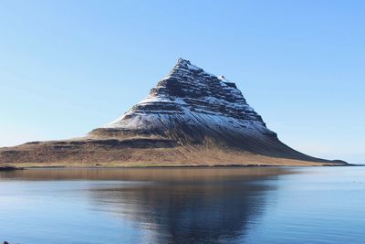 Scenic view of sea by mountain against blue sky