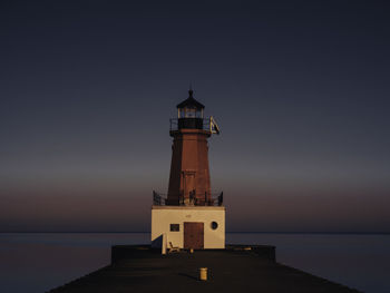 Lighthouse by sea against sky during sunset