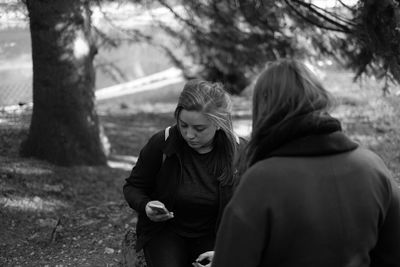 Woman using mobile phone while sitting with friend at park