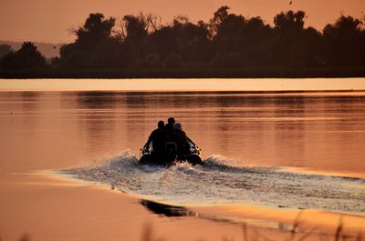 Silhouette men in lake against sky during sunset