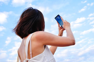 Rear view of woman using mobile phone against sky