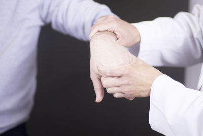 Midsection of doctor examining hand against black background