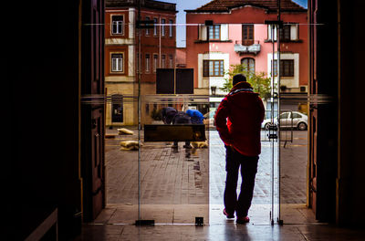 Rear view of man walking on alley amidst buildings in city