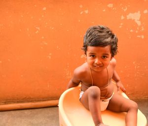 Portrait of smiling boy sitting against orange wall