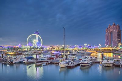 Illuminated ferris wheel at harbor against sky