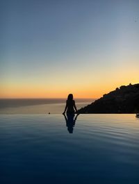 Silhouette man on sea against sky during sunset