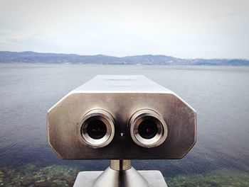 Close-up of coin-operated binoculars by sea against sky