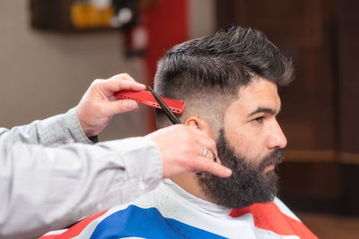 Cropped hands of barber cutting male customer hair with scissors in salon